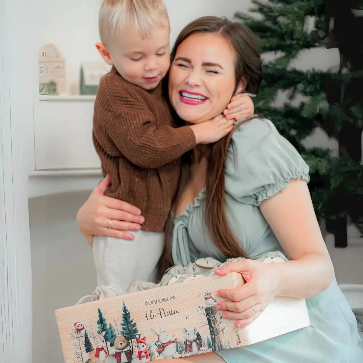 Mutter und Tochter öffnen gemeinsam ein Türchen am personalisierten Adventskalender - familiäres Weihnachtserlebnis mit selbstbefülltem Holzkalender im festlich dekorierten Wohnzimmer