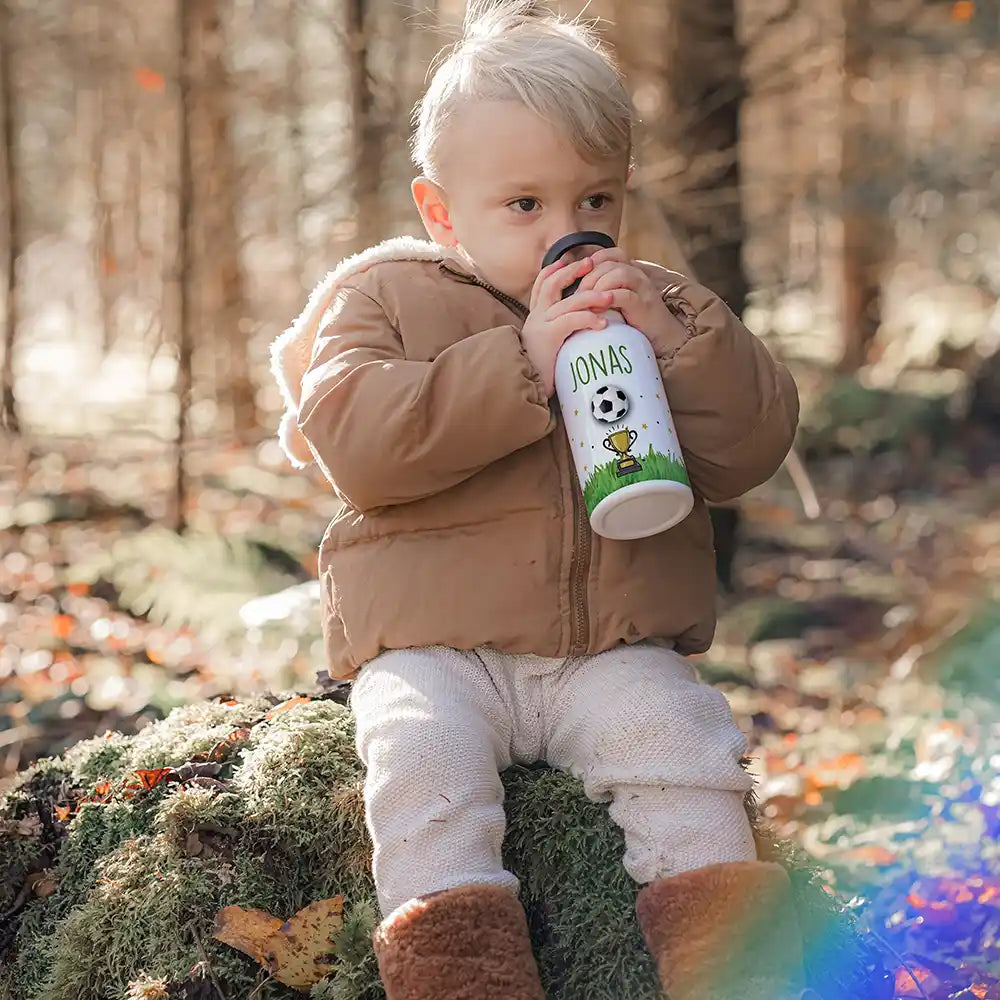 Enfant buvant à sa gourde personnalisée motif Football et trophée en forêt — Kidsmood
