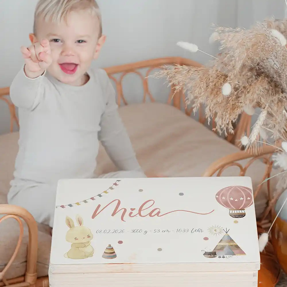 Boîte à souvenirs bébé personnalisée Lapin et montgolfière – enfant souriant à côté du coffret personnalisé